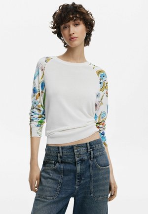 Maglione bianco con maniche a fantasia floreale, scollo rotondo e polsini a costine, abbinato a jeans in denim a vita alta con diverse tasche anteriori.
