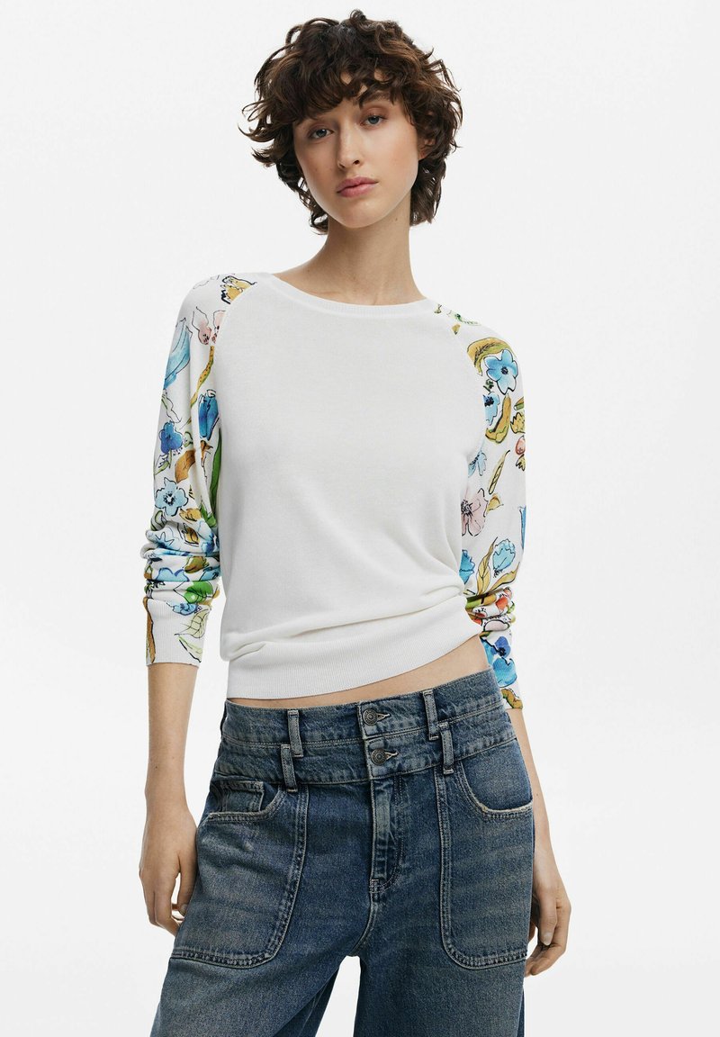 Maglione bianco con maniche a fantasia floreale, scollo rotondo e polsini a costine, abbinato a jeans in denim a vita alta con diverse tasche anteriori.