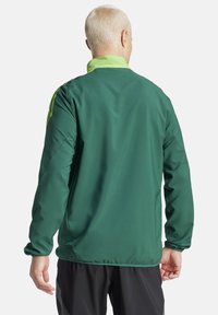 Veste coupe-vent verte avec un grand col, des accents de vert clair contrastants et des manches longues ; texture lisse et design ajusté.