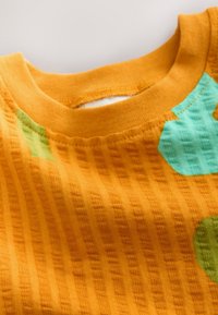 Tejido texturizado naranja con un diseño acanalado y formas irregulares en tonos menta y verde, creando un patrón vibrante y alegre.