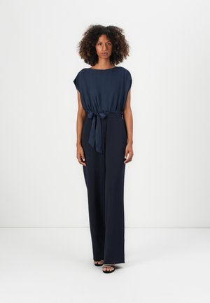 Combinaison bleu marine avec des manches courtes et une ceinture à nouer à la taille. Présente une coupe décontractée et un design de pantalon large et fluide.