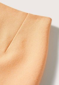 Gros plan sur un tissu texturé couleur pêche avec une couture verticale et une légère ombre sur un fond clair.