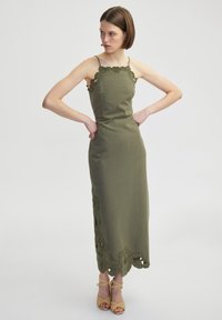 Oliwkowa maxi sukienka na ramiączkach, z koronkowym wykończeniem przy dekolcie i wyciętymi kwiatowymi akcentami wzdłuż dołu.