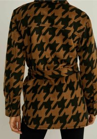 Giacca a motivo houndstooth marrone e verde con vita cintata, polsini arrotolati e colletto. Tessuto morbido e strutturato con un design classico.