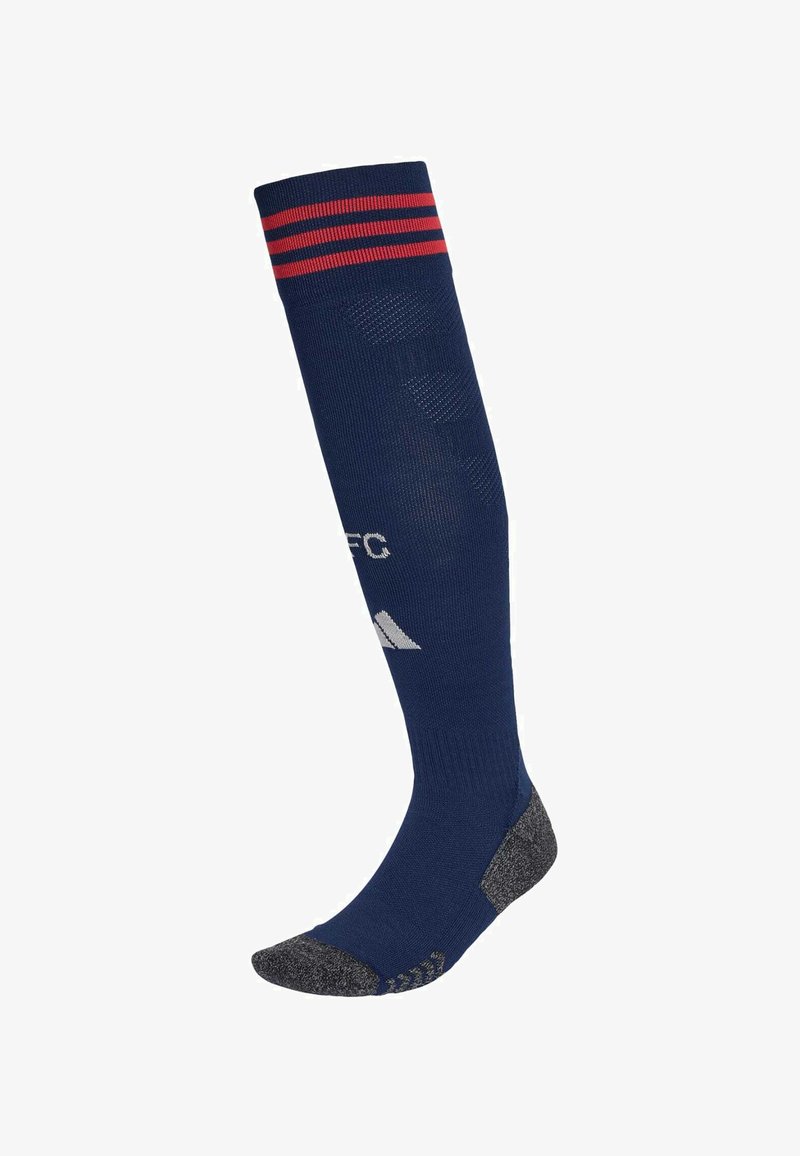 Calcetín deportivo azul marino hasta la rodilla con rayas rojas en la parte superior, plantilla texturizada gris y logotipo blanco en la espinilla.