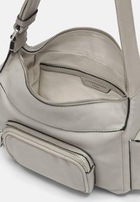 Skórzana torba w jasnoszarym kolorze o gładkiej fakturze. Posiada główną komorę zapinaną na zamek oraz zewnętrzną kieszeń, obie wyłożone materiałem.