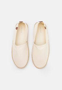 Beige kanvaskengät espadrilles, joissa on kudottu juteepohja. Liukuvat mallit, joissa on ruskea nahka-akseli kantapäässä. Pehmeä rakenne.