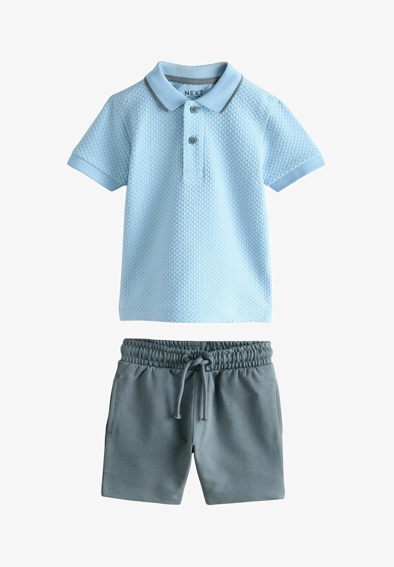 Polo de manga corta texturizado de color azul claro, combinado con pantalones cortos de cintura elástica en gris oscuro con cordón, dispuestos planos sobre un fondo blanco.