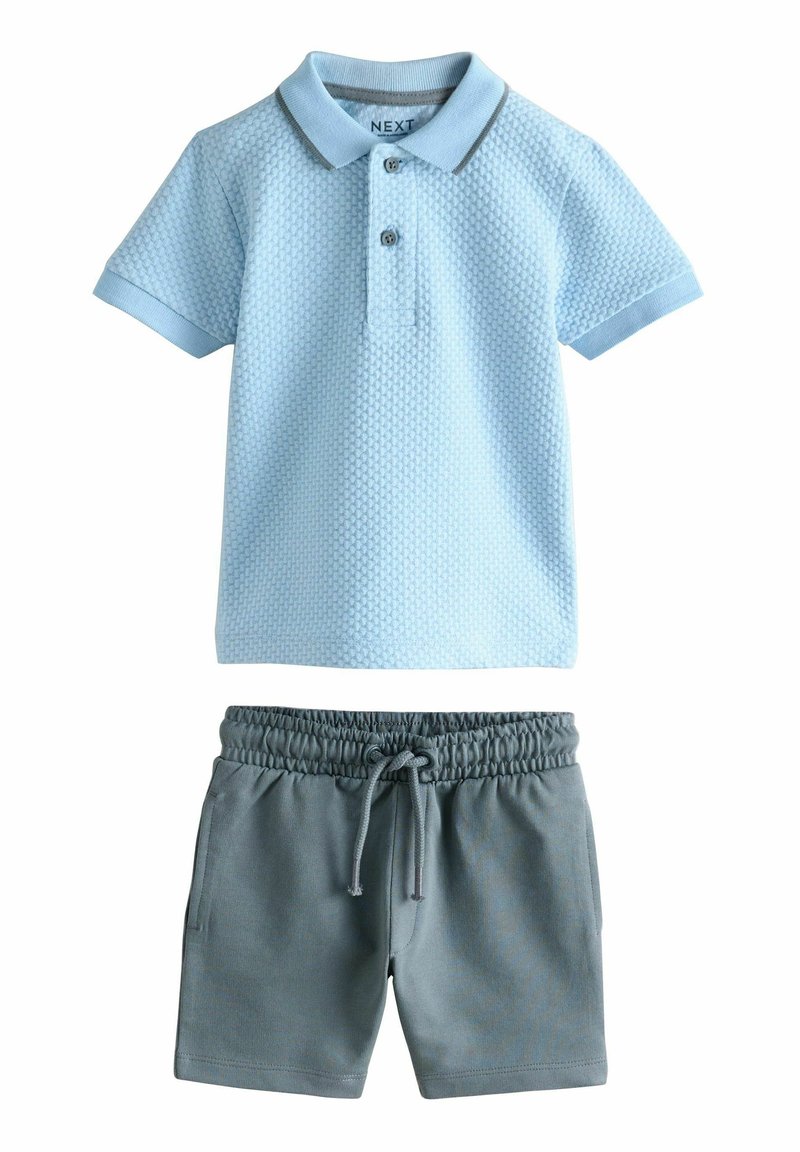 Tricou polo de culoare albastru deschis, cu un model texturat și guler contrastant, combinat cu pantaloni scurți gri, cu un braț elastic și buzunare laterale.