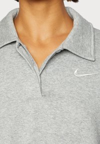 Grå polo t-shirt i mjukt material med en strukturerad yta, med en klassisk krage och en liten vit Nike-logotyp på vänster sida.