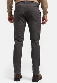 Pantalon gris texturé à coupe slim, avec un motif subtil, deux poches arrière et des accents de boutons marron. Porté avec des chaussures marron.