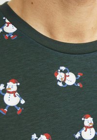 Grøn t-shirt af stof med et mønster af tegneserie-sne mænd iført røde hatte, hvide tørklæder og blå accenter. Rund hals design.