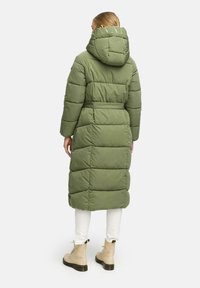 Cappotto imbottito lungo verde oliva con cappuccio, caratterizzato da un'imbottitura orizzontale, vita abbottonata e un logo sul colletto.