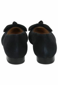Zapatos de ante negro con punta redondeada, que presentan un destacado lazo en la parte trasera y un tacón bajo y sólido. Textura suave en general.