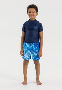 T-shirt de surf bleu à manches courtes, avec un design contrasté sur les épaules, assorti à un short de bain bleu arborant un motif marbré aquatique.
