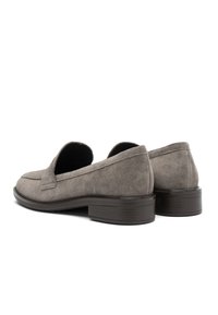 Gray suede loafers with a low, stacked heel, featuring a rounded toe and a decorative stitched apron detail. Smooth texture throughout.