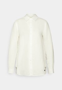 Camicia di lino bianca con maniche lunghe, chiusura frontale con bottoni, colletto aperto e spacchi laterali. Presenta un piccolo logo nero vicino all'orlo.