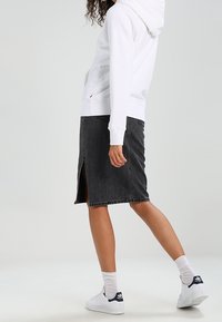 Felpa bianca con cappuccio abbinata a una gonna di jeans grigia al ginocchio con spacco frontale. Indossata con sneakers bianche e calzini al polpaccio.