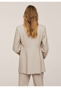 Jasnobeżowa, dopasowana marynarka o prostym kroju, z usztywnionymi ramionami, subtelnym prążkowanym wzorem oraz długimi rękawami ozdobionymi guzikami.