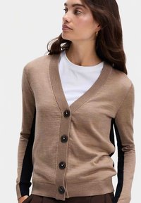 Beige cardigan lavet af blødt stof med V-hals, knaplukning, ribbede ærmekanter og kontrasterende sorte sidepaneler.