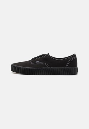 Czarny niski sneaker Vans z grubą żeberkową podeszwą, białym przeszyciem i czarnymi sznurówkami na gładkim jasnym tle, widok z boku.