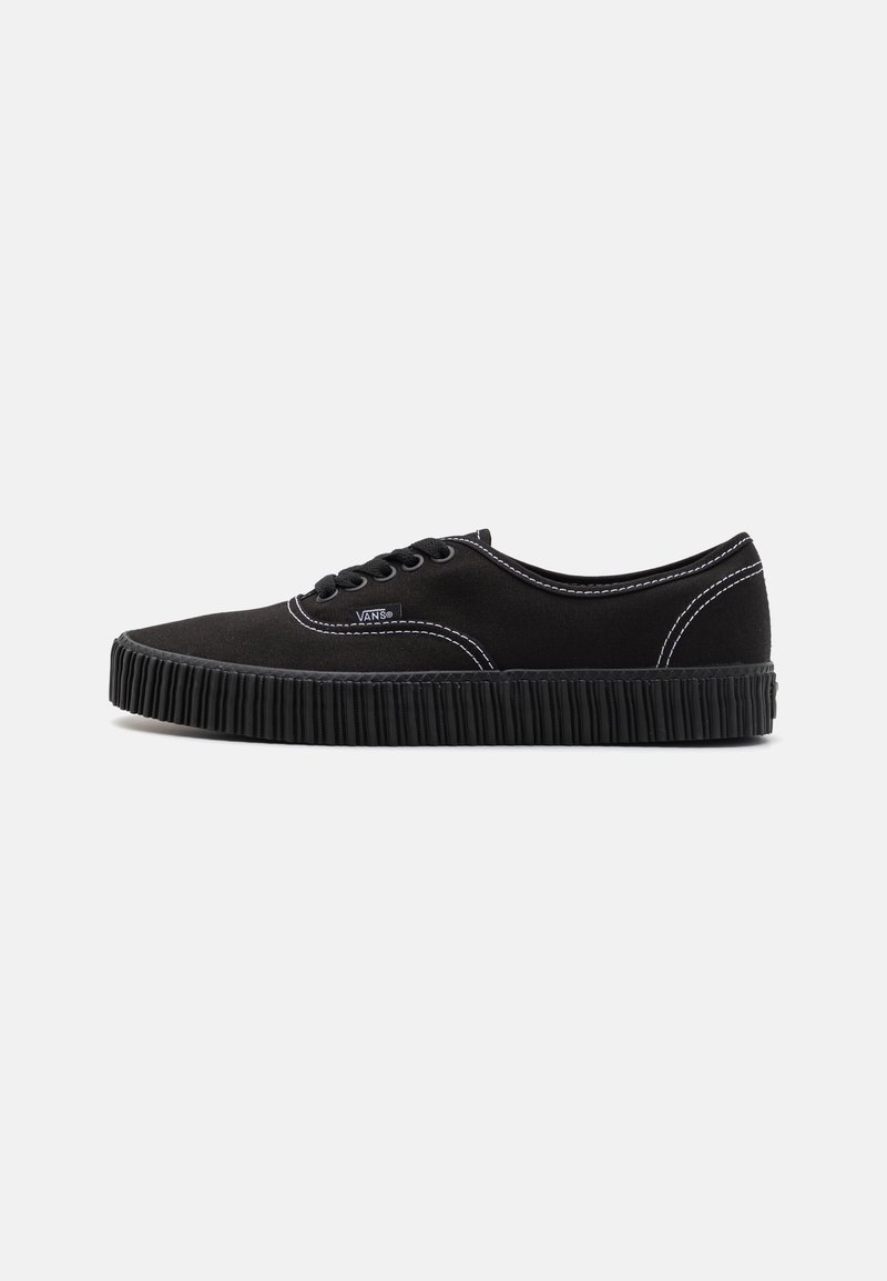 Baskets basses Vans noires avec semelle épaisse côtelée, coutures blanches et lacets noirs sur fond clair uni, vue de côté.