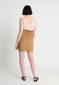 Tan mockaskjol med rynkig midja och bälte, i kombination med en ljusrosa tanktop. Slät textur, avslappnad design.