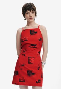 Röd ärmlös klänning i slätt material, med svart grafiskt tryck av ansikten och text, med en figursydd silhuett och rak nederkant.