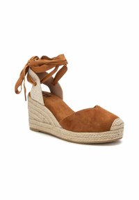 Espadrille de cuña de ante marrón con base de yute trenzado, que presenta una puntera cerrada y lazos ajustables en el tobillo de tela beige.