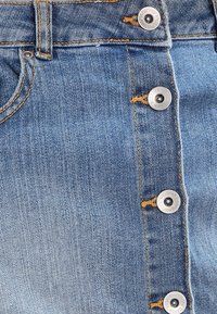 Jeanskjol i ljusblå färg med knappdesign framtill, synlig sömnad och metallknappar med varumärkesdetaljer.