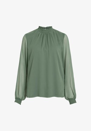 Zielona bluzka z wysokim, falbaniastym kołnierzem, długimi, przezroczystymi rękawami i elastycznymi mankietami. Tkanina wydaje się lekka o gładkiej fakturze.