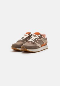 Bruine en beige sneakers met oranje accenten, uitgevoerd in een combinatie van suède en stof, met dikke witte veters en een gestructureerde rubberen buitenzool.
