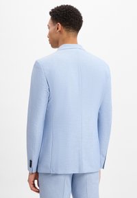 Hellblauer Anzugjacke mit strukturiertem Finish, einfacher Schlitz und geknöpften Bündchen, von hinten betrachtet. Ergänzende Schneiderarbeiten sichtbar.