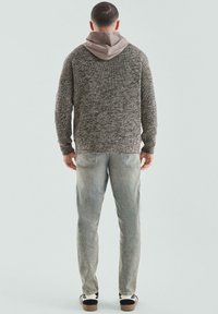 Sweter z dzianiny w ciemnoszarym kolorze z jasnoszarym kapturem, połączony z jasnymi, wyblakłymi dżinsami i czarnymi trampkami z białymi akcentami, widziany z tyłu.