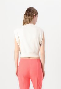 Ärmlös, kort topp i off-white bomullsblandning med ribbad fåll. Matchas med figurnära, knallrosa byxor. Enkel, ren design.