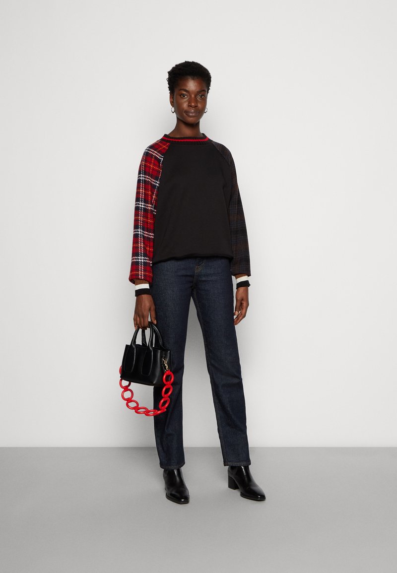 Czarny sweter z kraciastymi czerwono-granatowymi rękawami, noszony z ciemnymi dżinsami i czarnymi botkami za kostkę. W zestawie czarna torebka z czerwoną łańcuszkową rączką.