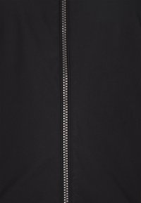 Zwarte jas met een centrale rits en een gestructureerde trekker, gemaakt van gladde stof. Geen opvallende patronen of extra accenten aanwezig.