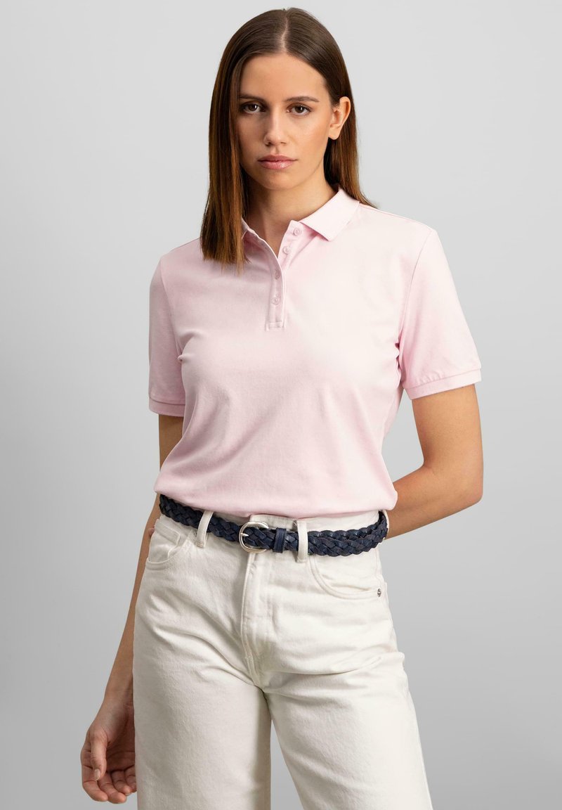 Jasnoróżowa koszulka polo z krótkimi rękawami, z kołnierzykiem i listwą na guziki. Połączona z białymi spodniami i plecionym granatowym paskiem.