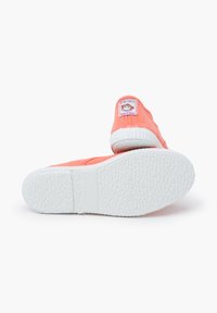 Scarpe in tela corallo con suole in gomma bianche, caratterizzate da un bordo cucito e un'etichetta intrecciata sul tallone che mostra una scimmia in stile cartone animato.