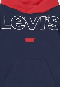 Navy blue hoodie with red accents, featuring a white "Levi's" logo and a red patch with the brand emblem. Includes a front pocket.