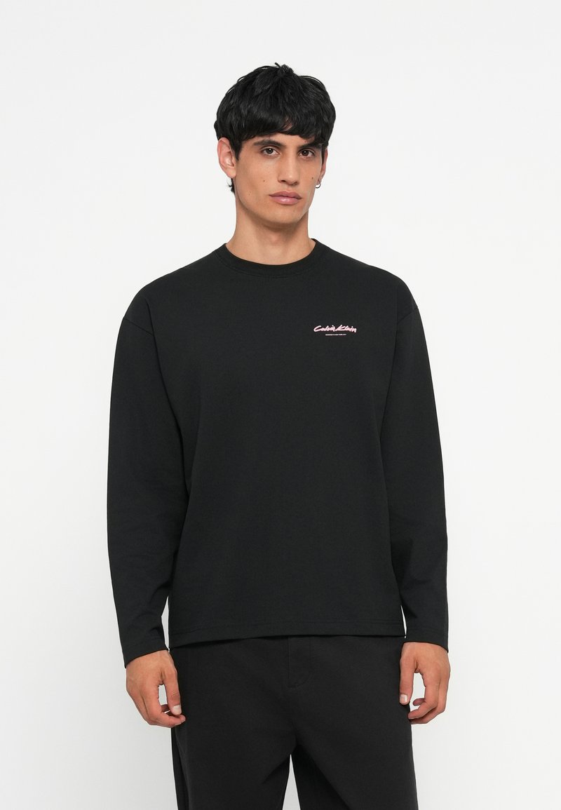 Schwarzes Langarm-T-Shirt aus Baumwolle mit Rundhalsausschnitt und kleinem pinken Logo auf der Brust. Standard, entspannter Schnitt.