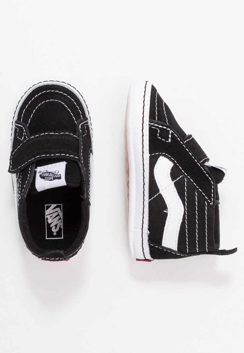 Baskets Vans pour tout-petits en noir et blanc avec des brides en velcro, des coutures blanches et un logo vague blanc sur le côté, vues du dessus et de côté.