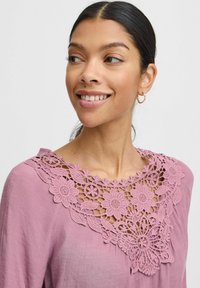 Bluse med blondekant i blød pink med blomsterdesign omkring halsudskæringen. Letvægtsstof med en afslappet pasform og lange ærmer.