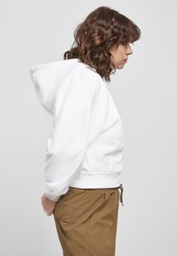 Felpa bianca con cappuccio regolabile, polsini a coste e vestibilità rilassata, abbinata a pantaloni cargo marrone chiaro con tasche laterali.