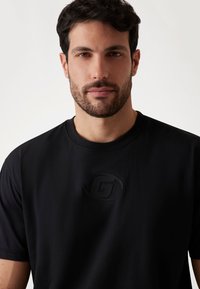 Sort T-shirt med korte ærmer, lavet af glat stof, med et præget logo på brystet, rund halsudskæring og en afslappet pasform.