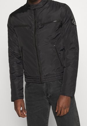 Veste bombardier noire en matériau lisse et léger, dotée de deux poches zippées sur la poitrine, de poignets côtelés et d'une taille ajustée.