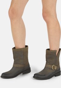 Botas de tobillo de cuero marrón con un acabado mate, que presentan una hebilla lateral, un eje ligeramente caído y un tacón bajo apilado.