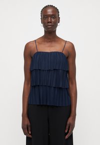 Navy blue pleated top with three layered ruffles, thin spaghetti straps, and a straight hem. Fabric has a smooth texture.