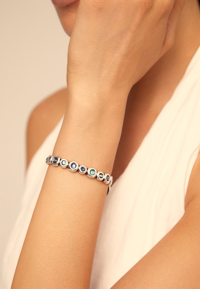 Bracelet en argent avec des pierres circulaires bleues et turquoise, alternant dans le design, présentant une surface lisse et polie et des sertissages ronds.