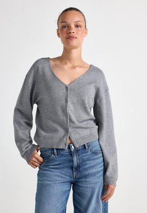 Grijze cardigan met een diepe V-hals, knoopsluiting en geribbelde zoom. Draagt over hooggekropte blauwe spijkerbroeken, met een ontspannen pasvorm en zachte textuur.